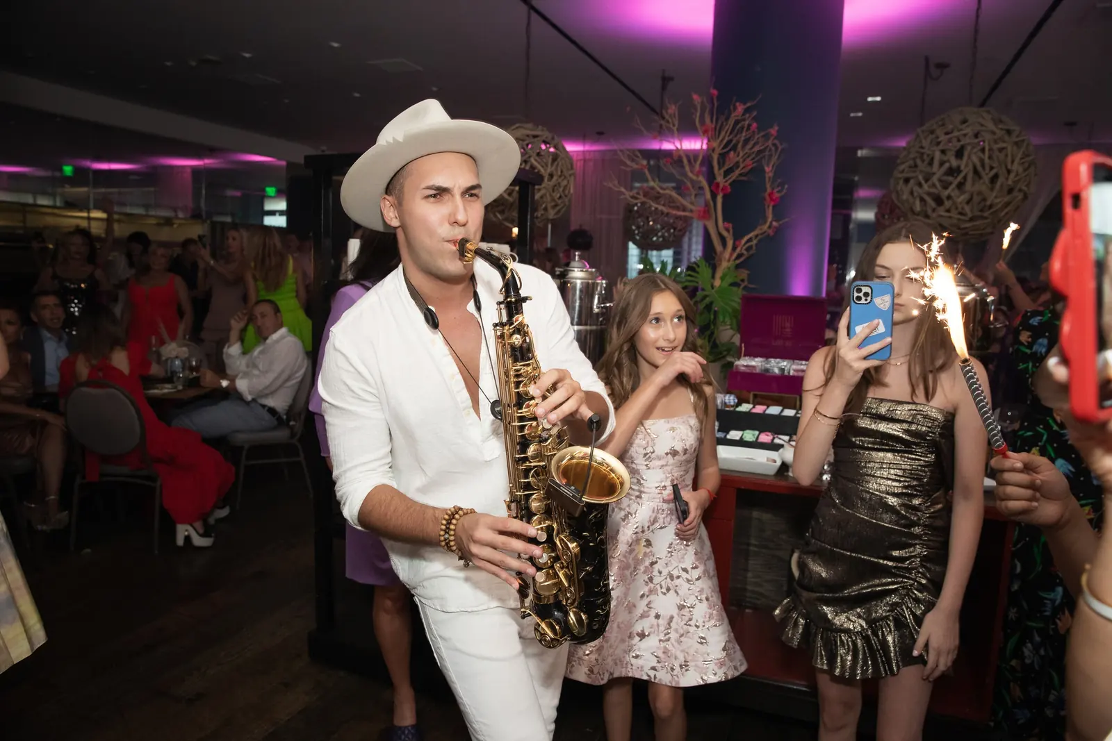 Saxophonist in white playing among guests with sparklers