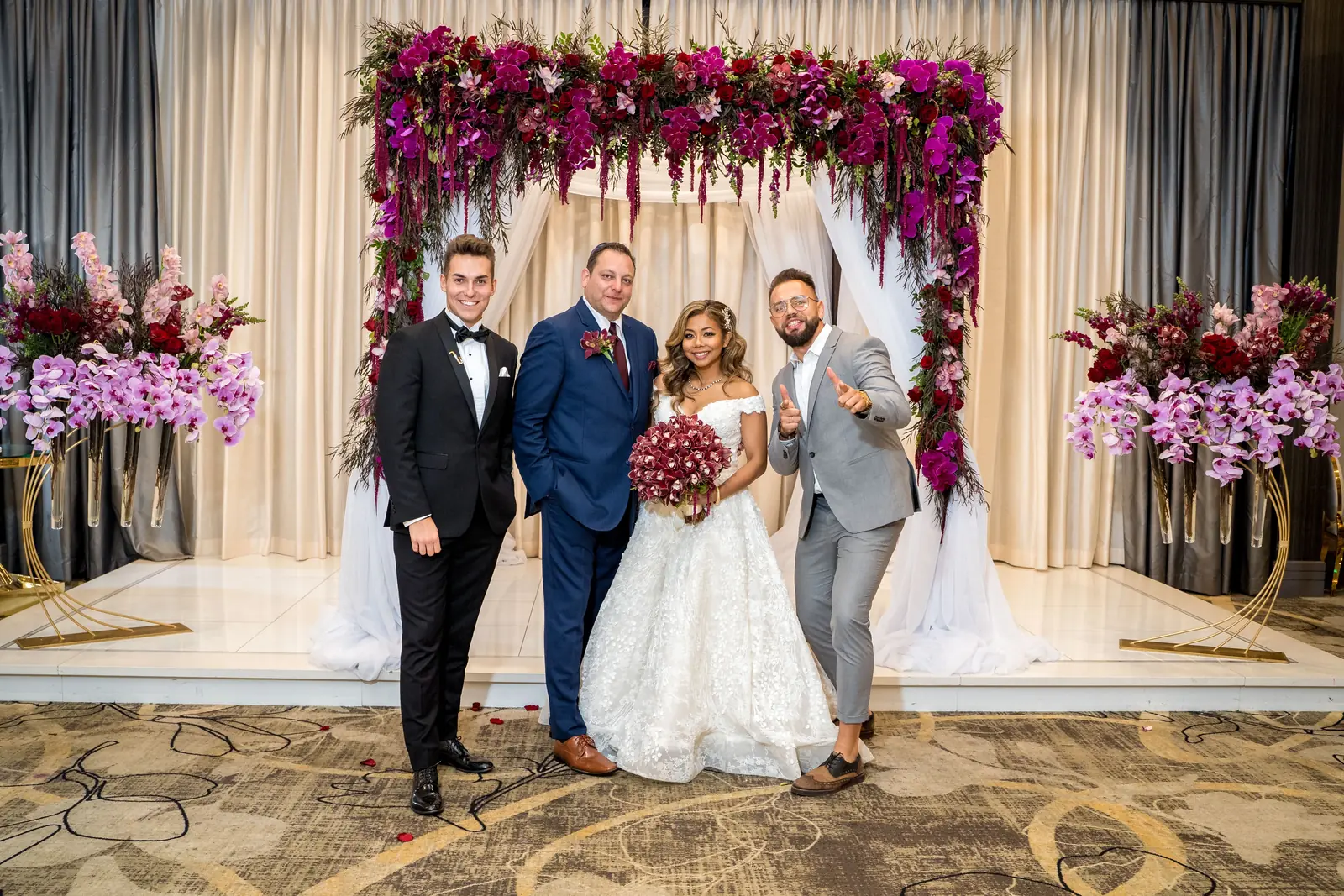 Wedding party gathered under a floral arch at the ceremony